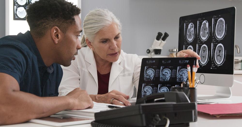 Doctora revisando con un paciente im&aacute;genes de resonancia magn&eacute;tica en una pantalla