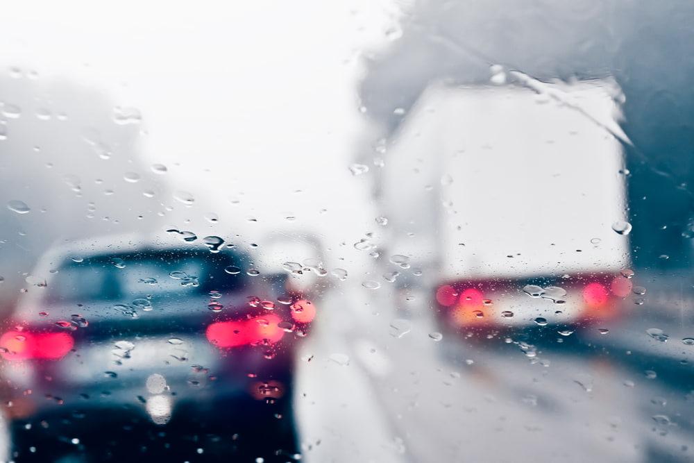 Tr&aacute;fico detenido visto a trav&eacute;s de un parabrisas mojado por la lluvia con luces de freno encendidas