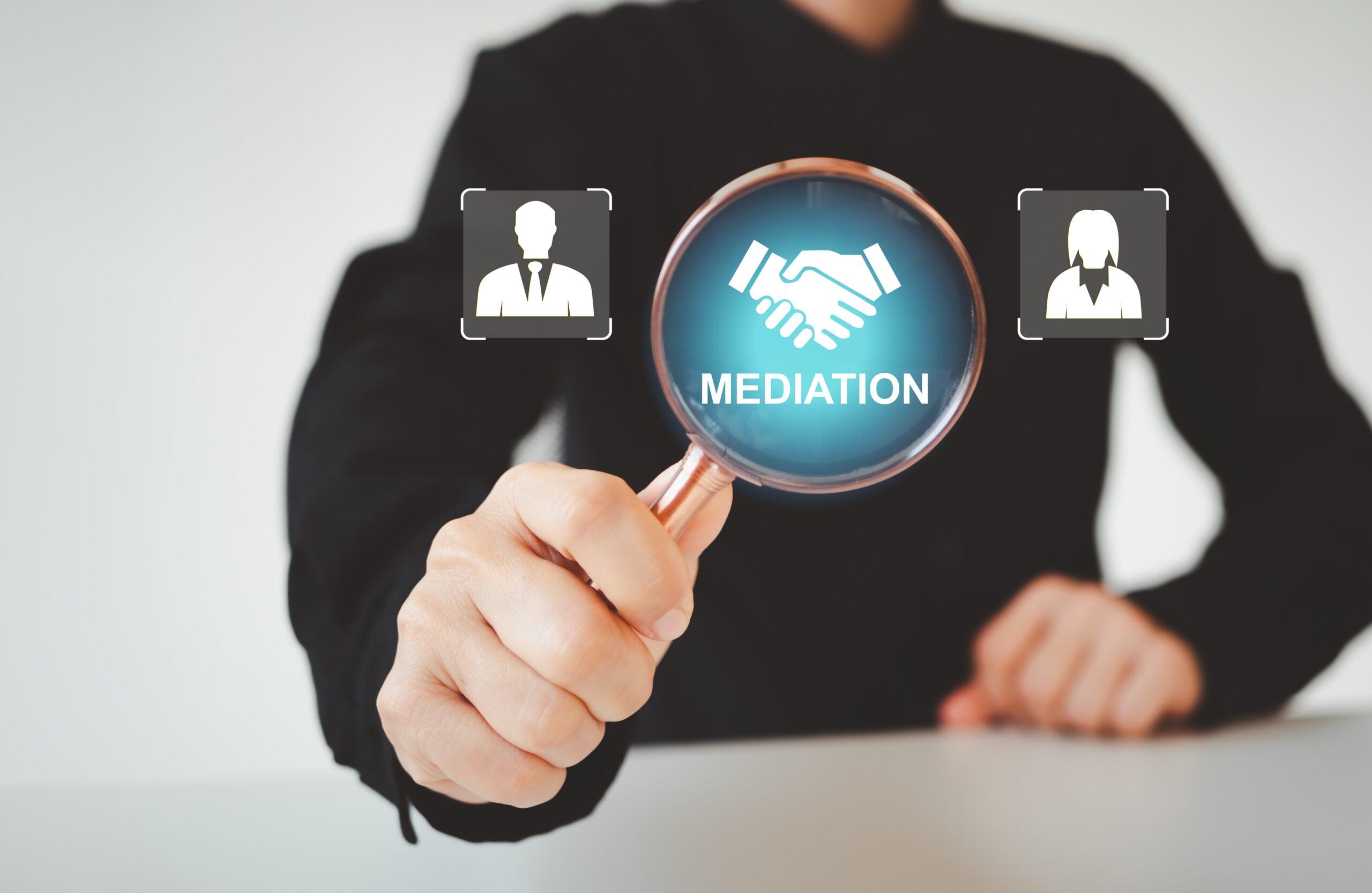 Mano sosteniendo una lupa sobre el &iacute;cono de un apret&oacute;n de manos con la palabra Mediation