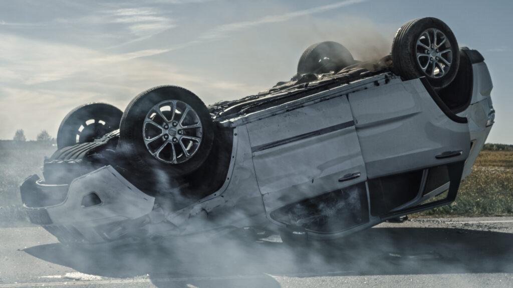 Camioneta plateada volcada con las llantas hacia arriba y humo alrededor en la carretera
