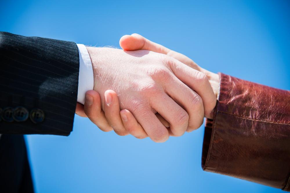Two people in business clothes shaking hands against a blue sky