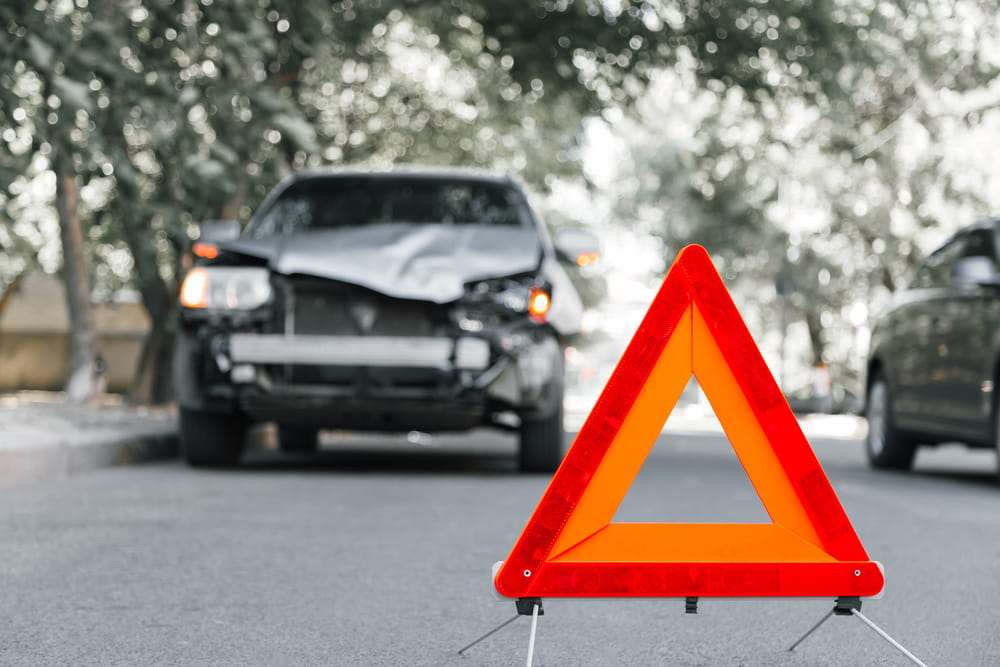 Red warning triangle set up on the road in front of a damaged black car, representing a hit and run accident in Houston