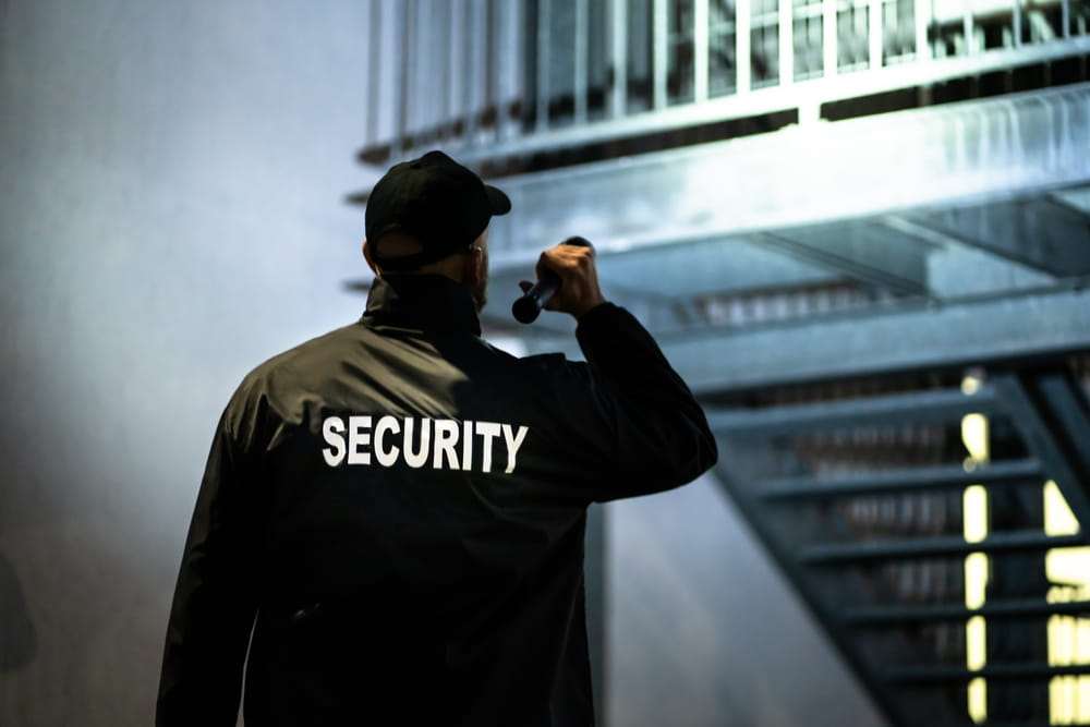 Guardia de seguridad de espaldas revisando con una linterna las escaleras exteriores de un edificio de noche