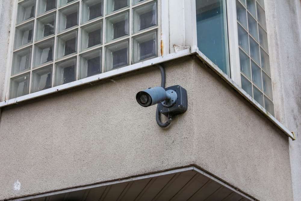 Cámara de seguridad instalada en la esquina exterior de un edificio con ventanas de bloques de vidrio