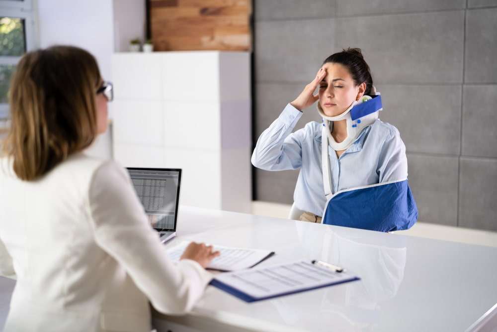 Woman wearing a neck brace and arm sling meeting with a personal injury lawyer after an accident.

