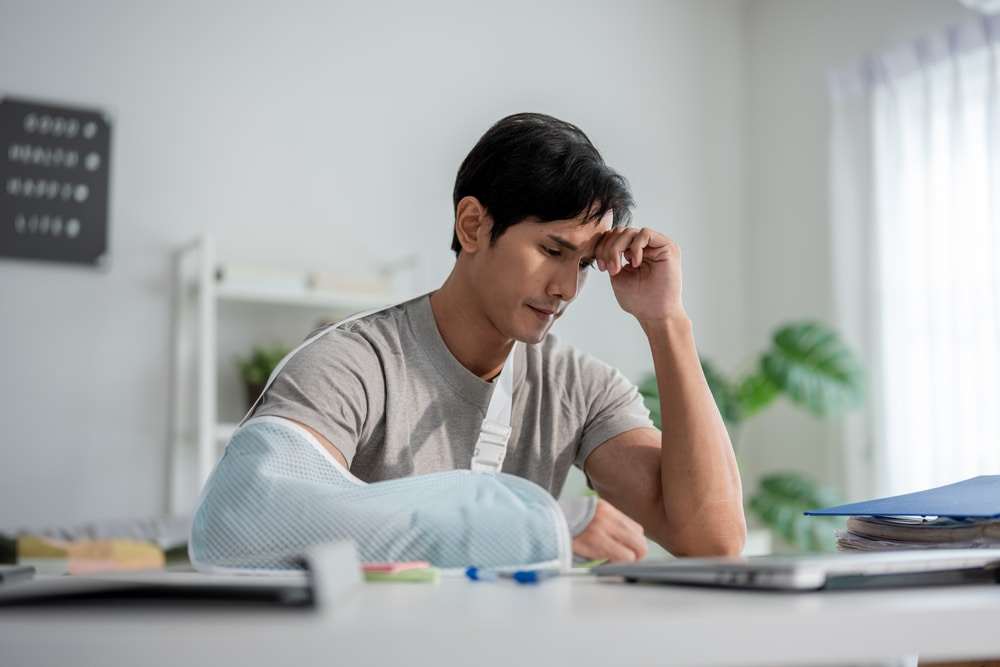 Man wearing an arm sling reviewing medical bills and expenses while recovering from injuries after an accident.

