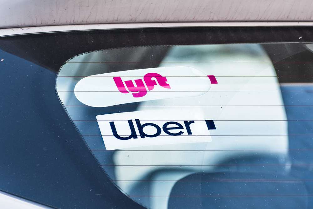 Uber and Lyft rideshare decals displayed on the rear window of a vehicle.
