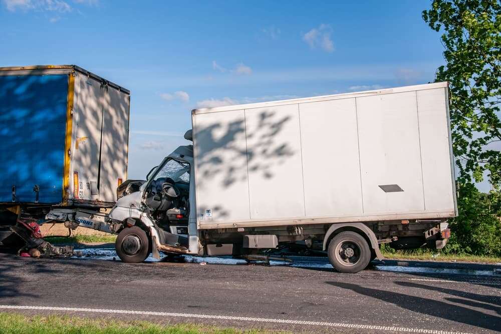 Box truck with severe front-end damage after colliding with the rear of a semi-trailer.