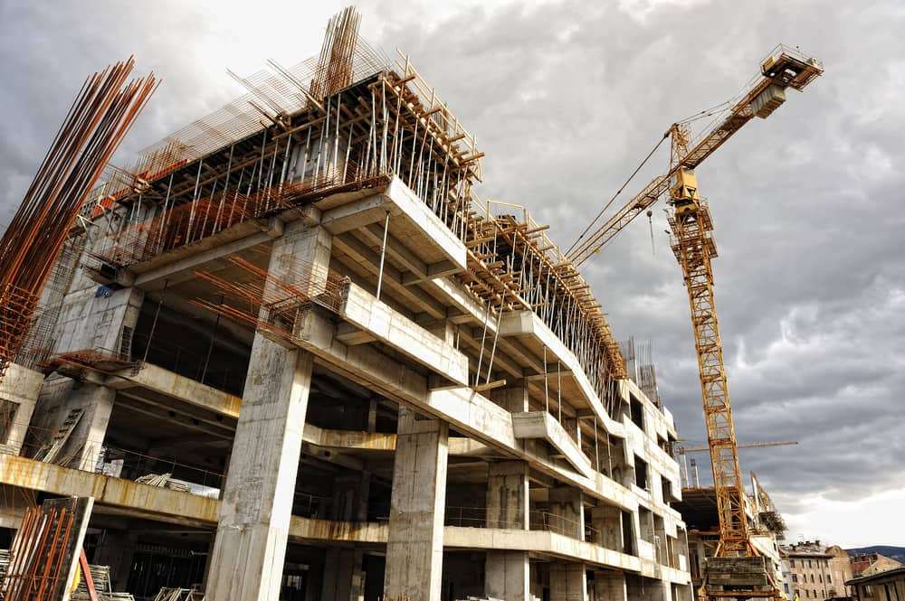 Concrete building under construction with a tower crane against a cloudy sky