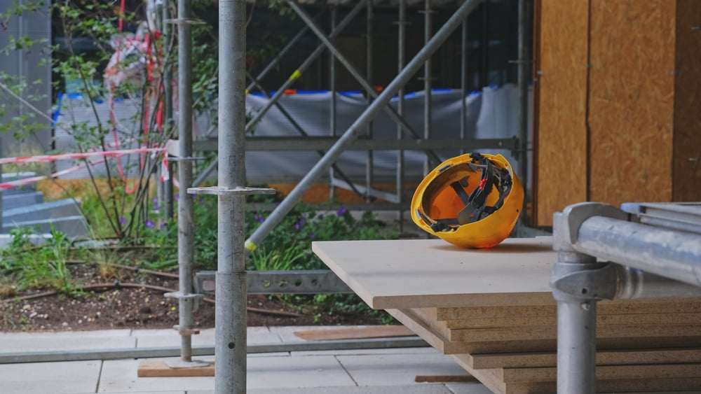 Yellow construction hard hat resting on building materials at an active construction site with scaffolding.