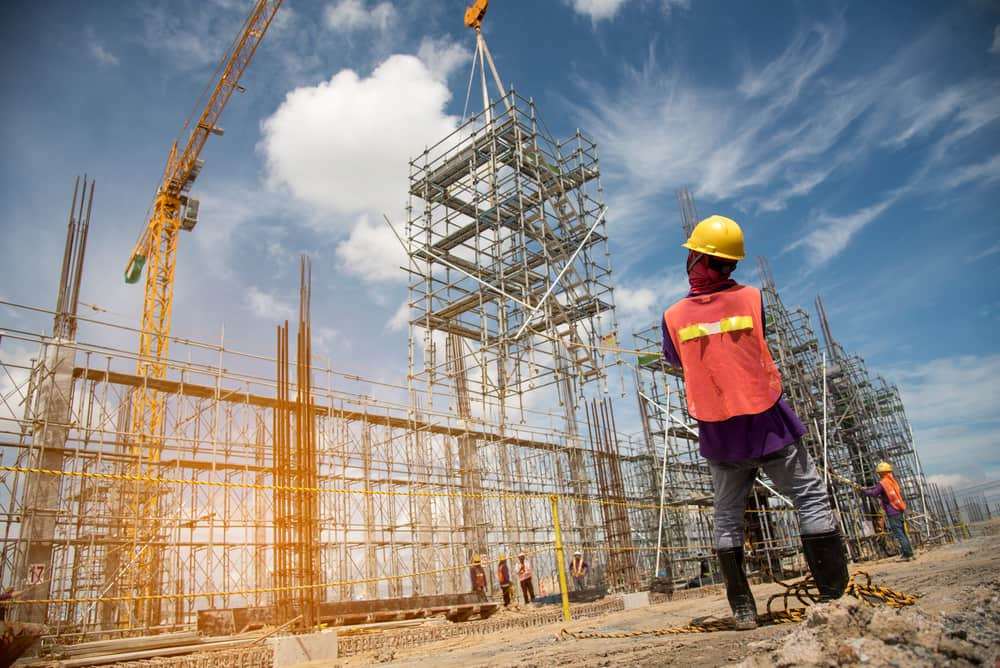 Construction workers operating around scaffolding and a tower crane at an active commercial construction site.