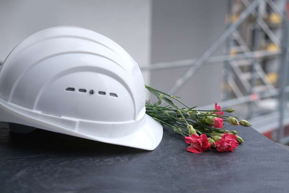 Construction hard hat and flowers placed as a memorial following a fatal workplace accident.

