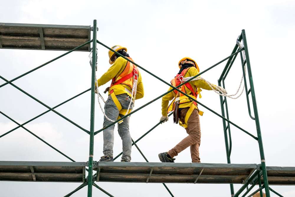 Construction workers wearing safety harnesses while working on elevated scaffolding at a job site.