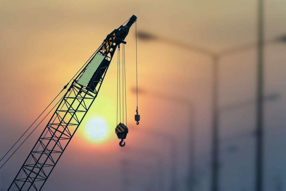Grúa de construcción con el gancho colgando frente al sol del atardecer