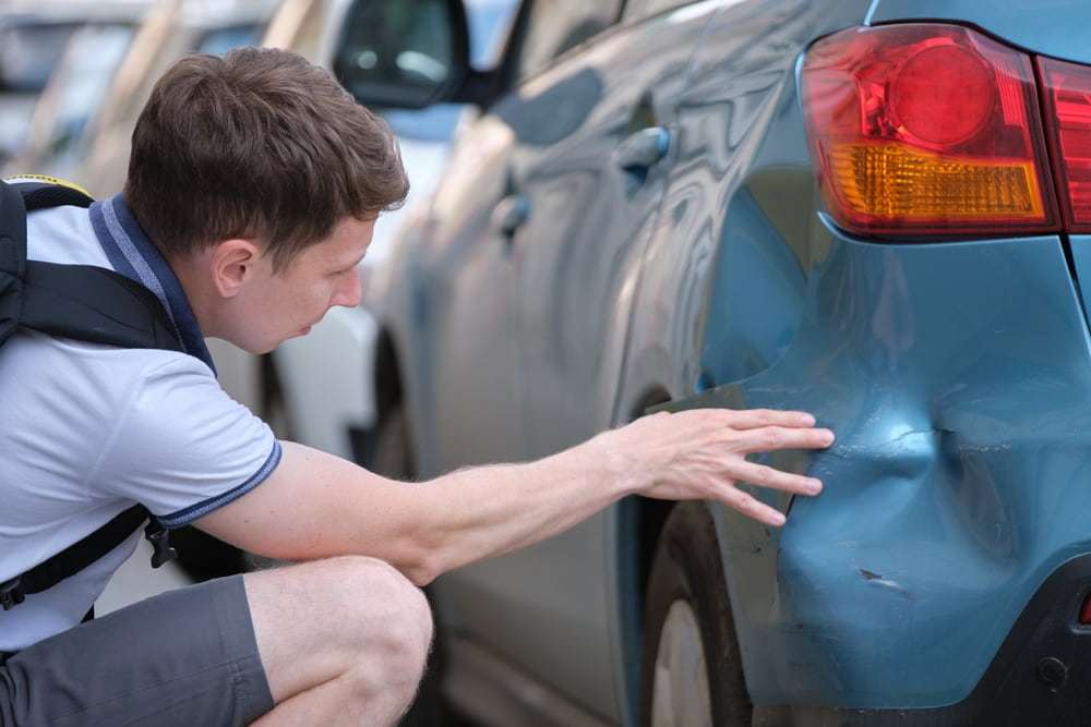 Driver examining damage to a vehicle’s rear bumper after a car accident.