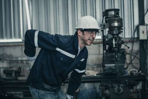 Factory worker holding his lower back in pain in a machine shop