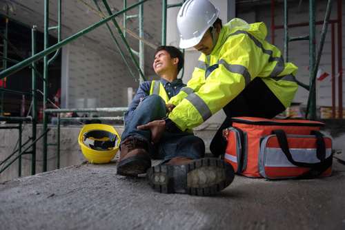 Worker giving first aid to an injured coworker's leg at a construction site