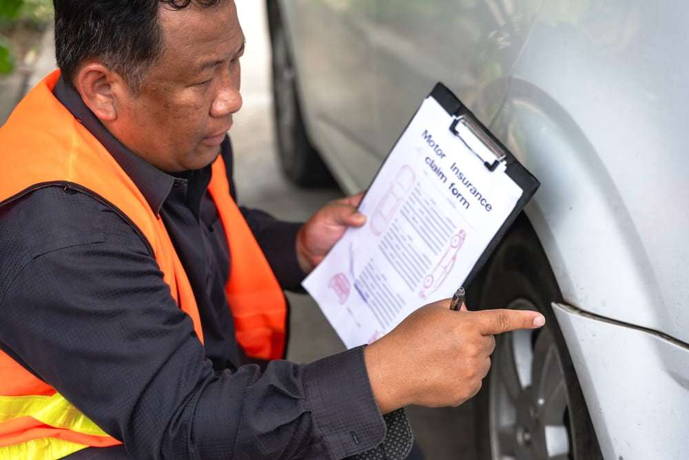 Insurance adjuster examining vehicle damage and documenting a motor vehicle insurance claim after an accident.