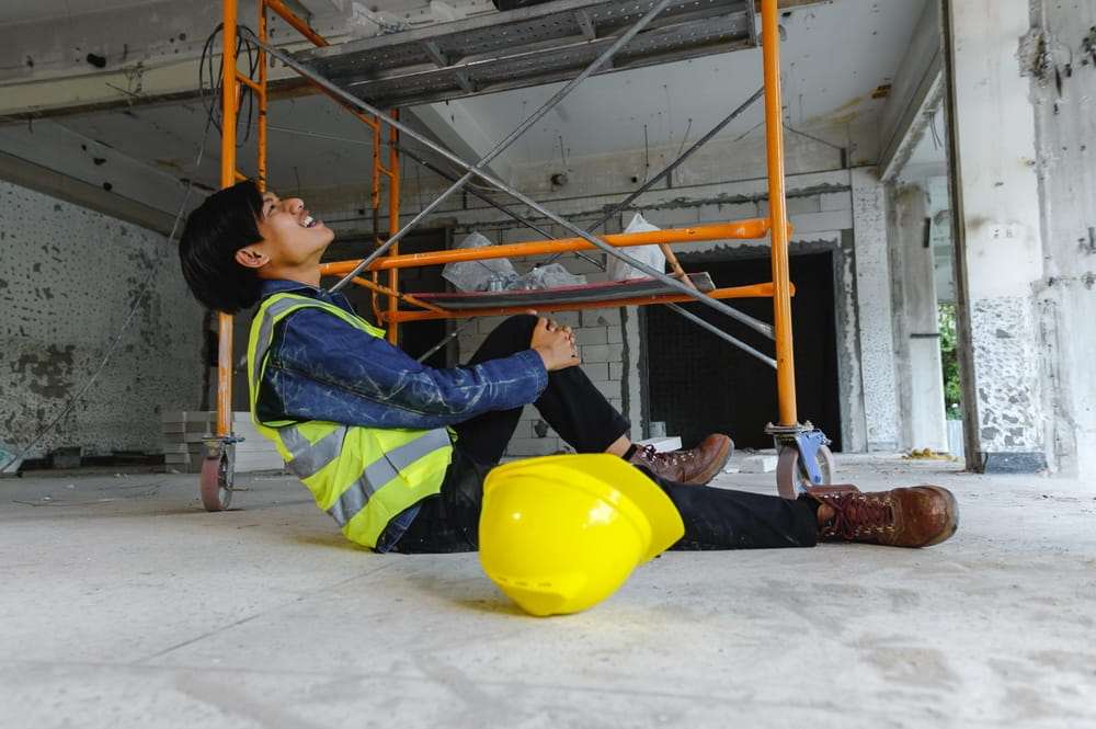 Trabajador de la construcci&oacute;n lesionado sentado junto a un andamio y un casco amarillo en el suelo, ilustrando una lesi&oacute;n de trabajo en Texas