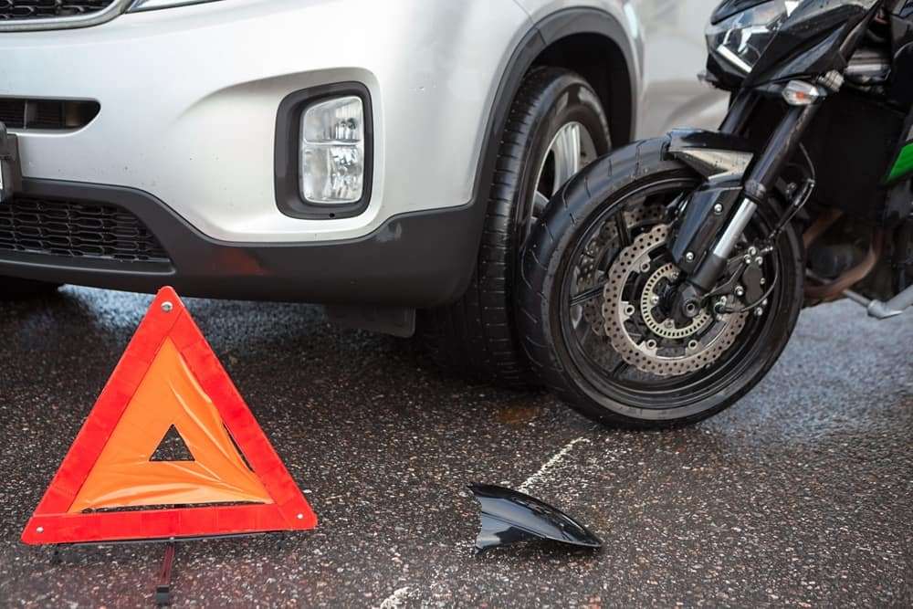 Motorcycle involved in a collision with an SUV at an intersection with a warning triangle marking the crash scene.