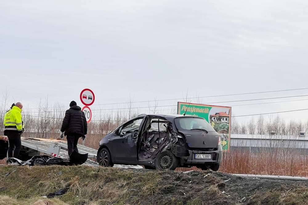 Dark car with a destroyed side on the roadside while an officer checks the scene