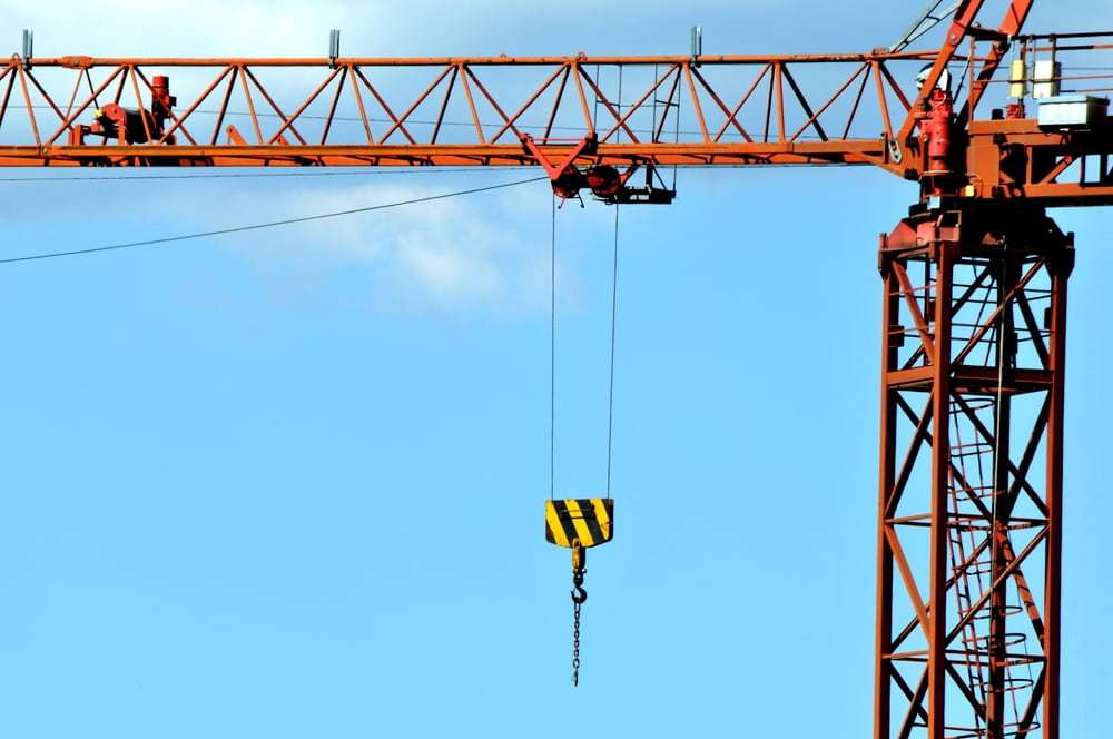 Tower crane with suspended lifting hook used to move heavy materials at a construction site.