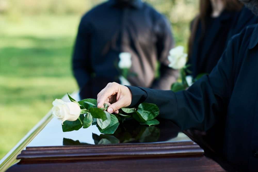 Mourner placing a white rose on a casket during a funeral following a wrongful death.