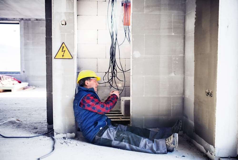 Electricista con casco amarillo tirado en el piso junto a cables sueltos