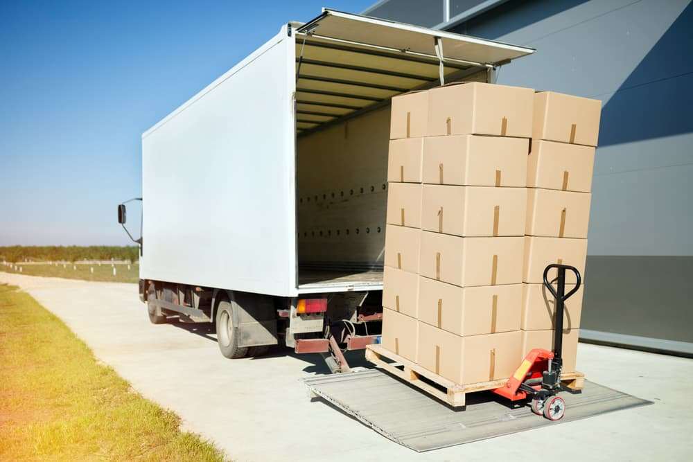 Delivery truck unloading a pallet of boxed goods with a pallet jack at a loading area