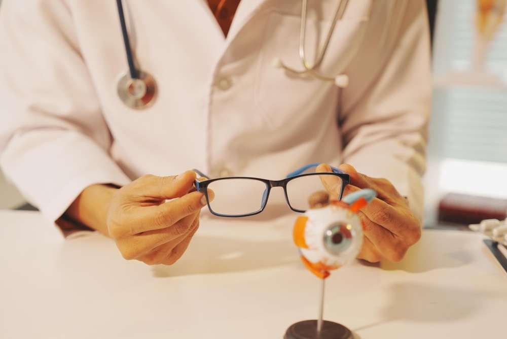 eye doctor holding a pair of eyeglasses behind an anatomical eye model during a vision examination