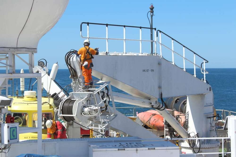 Maritime worker wearing safety gear performing maintenance on equipment aboard a vessel