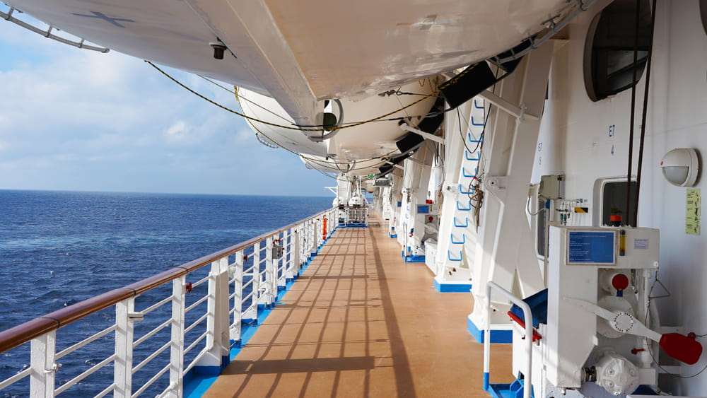 Exterior deck of a cruise ship with lifeboats and ocean views along the passenger walkway
