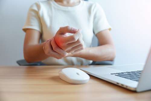person at a desk holding a painful wrist while working at a computer