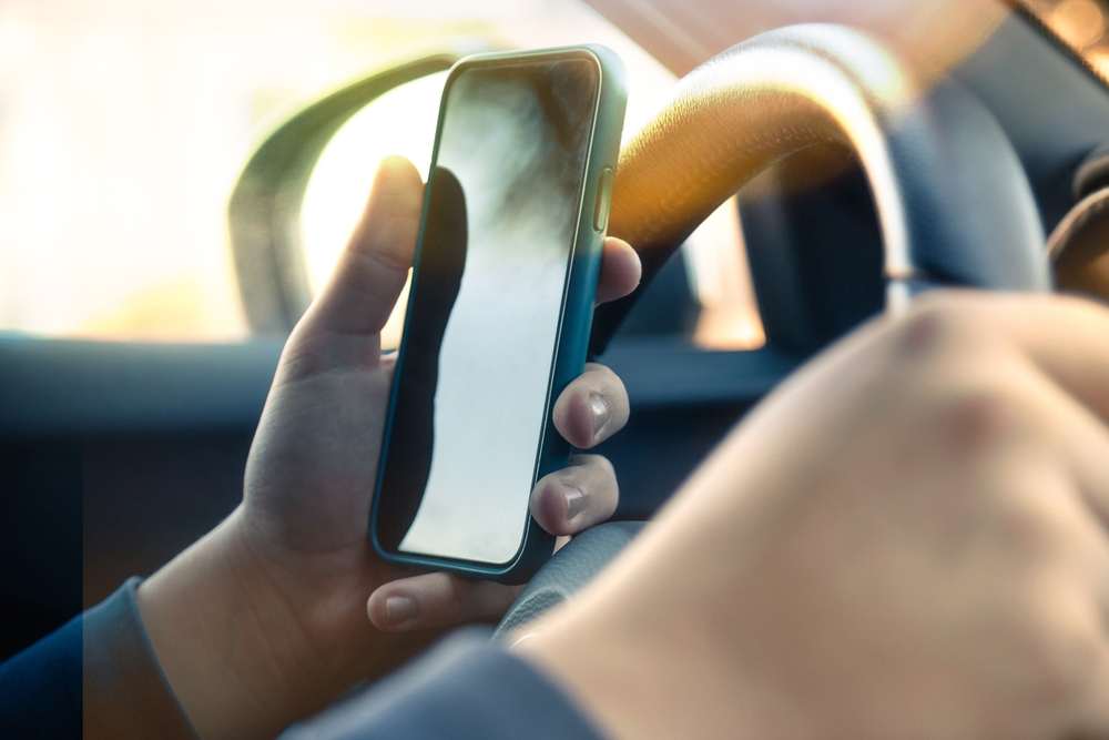Conductor sosteniendo un celular con una mano mientras maneja con la otra