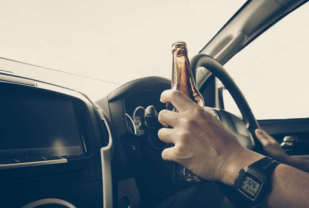 Conductor sosteniendo una botella de cerveza mientras maneja con la otra mano en el volante