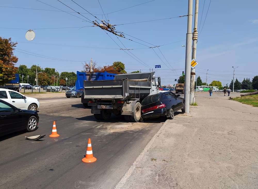 Black car crashed into the back of a dump truck on a city street with orange traffic cones on the pavement