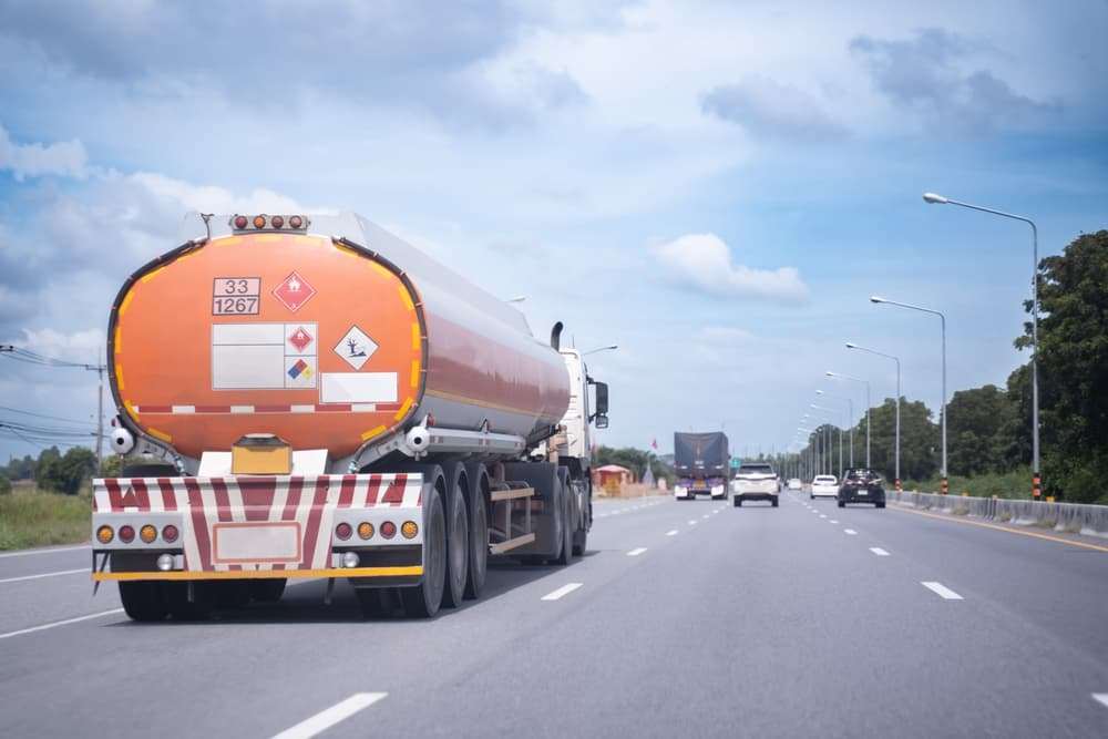 Orange fuel tanker truck with hazardous materials placards driving on a multi-lane highway