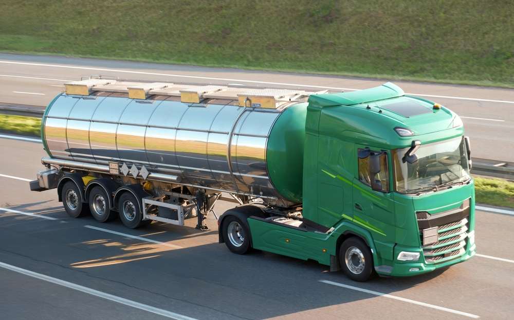 Green tanker truck with a stainless steel tank driving on a highway