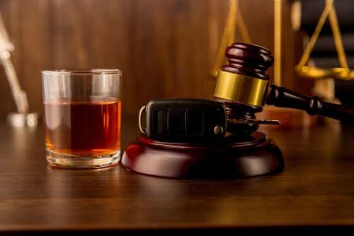 Mazo de juez con las llaves de un carro junto a un vaso de whisky en una mesa de madera
