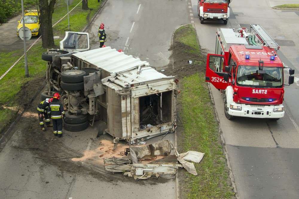 Dump truck tipped on its side on a city street while firefighters respond next to their red fire truck