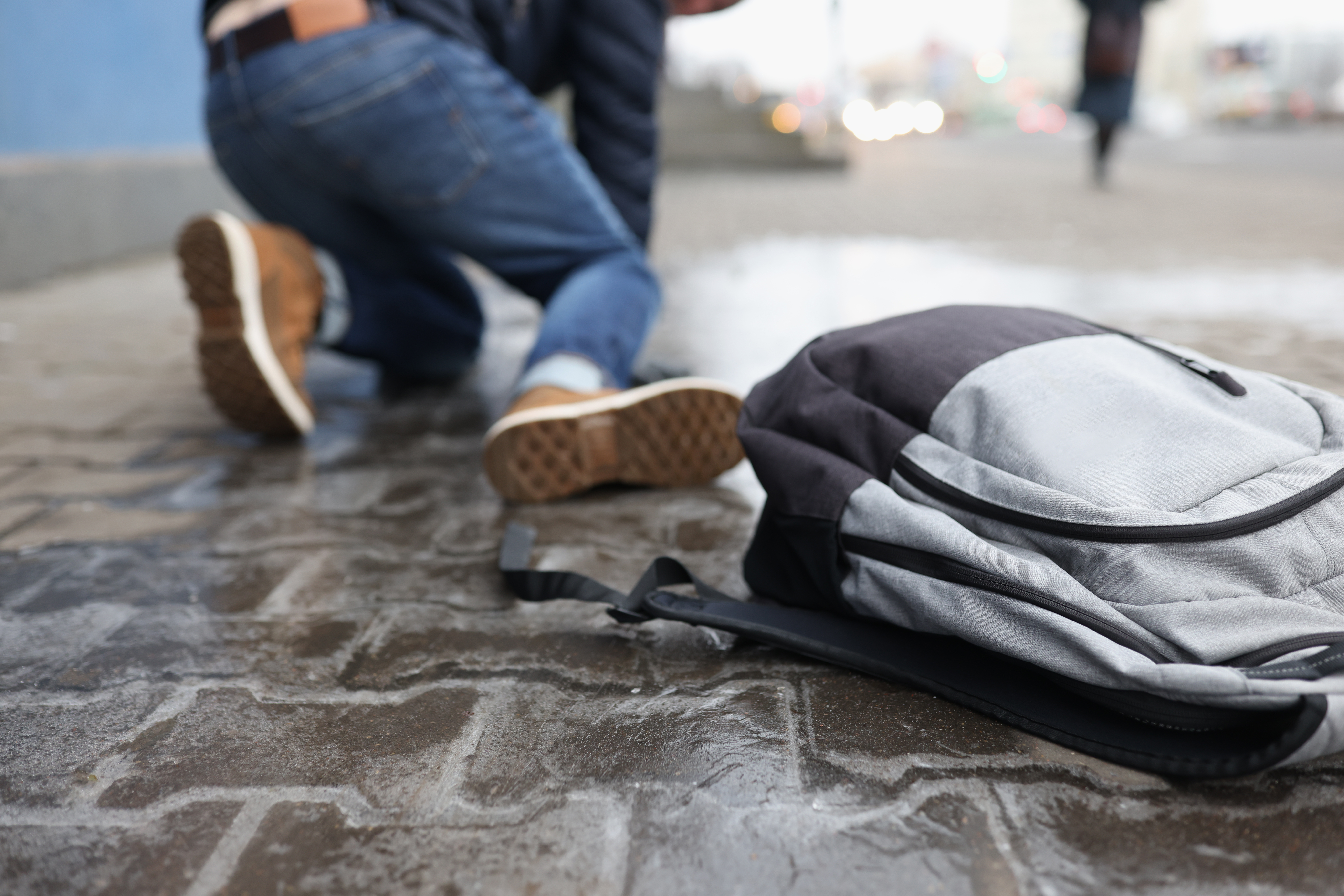 Man has fallen and dropped his backpack due to distraction from cell phone while walking