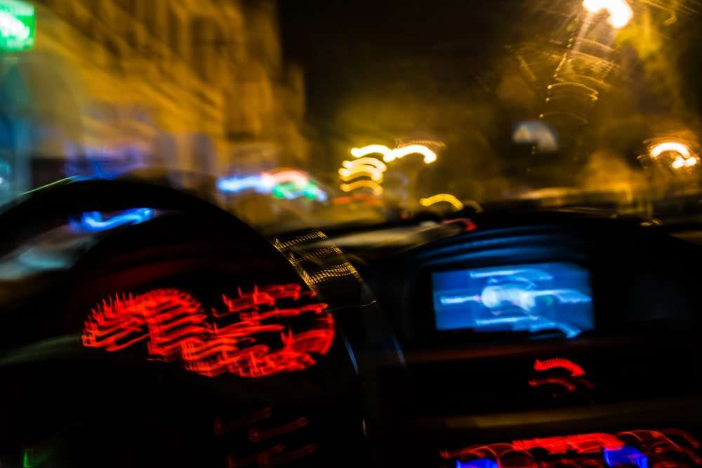 Vista borrosa desde el asiento del conductor de un tablero y las luces de la calle de noche